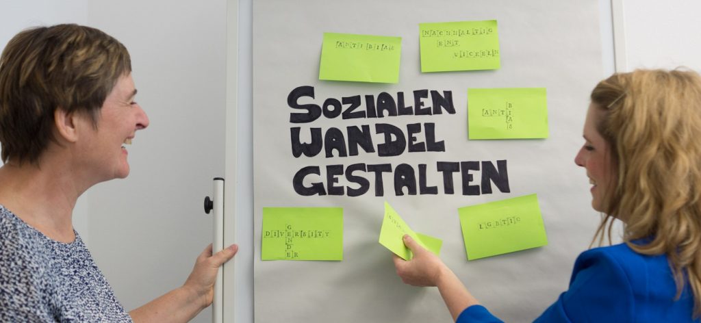 Zwei Frauen vor einem Flipchart, lachend
